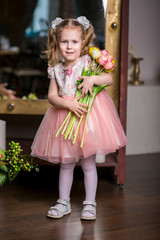 blue-eyed cute girl in a pink dress holding in her hands an armful of tulips