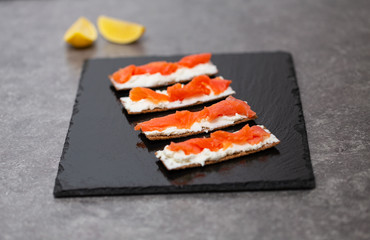 Tasty snack with salmon and soft cheese on a black plate