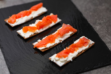 Tasty snack with salmon and soft cheese on a black plate
