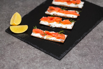 Tasty snack with salmon and soft cheese on a black plate