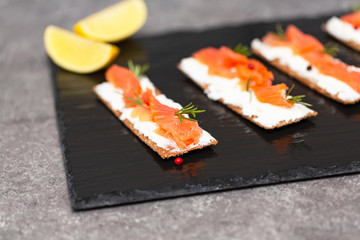 Tasty snack with salmon and soft cheese on a black plate