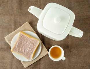 Morning breakfast with sweet mashed taro on a single slice of white bread and a teapot with tea.