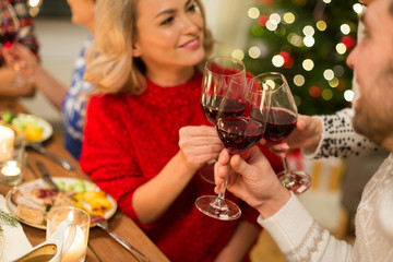 holidays and celebration concept - close up of happy friends having christmas dinner at home, drinking red wine and clinking glasses