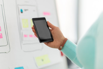 technology, user interface design and people concept - hand of ui designer or developer holding smartphone at office