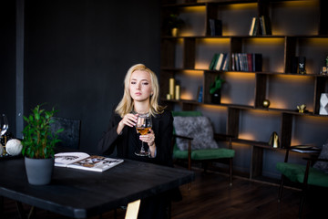 A beautiful young girl is sitting at the table in a jacket with a glass of wine in her office. Business concept