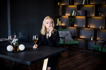 A beautiful young girl is sitting at the table in a jacket with a glass of wine in her office. Business concept