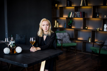 A beautiful young girl is sitting at the table in a jacket with a glass of wine in her office. Business concept
