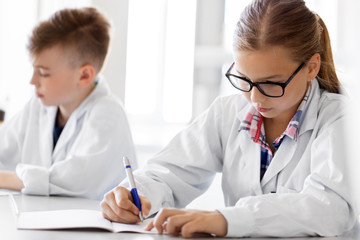 education, science and children concept - close up of girl studying chemistry at school laboratory and writing to workbooks