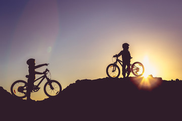 Silhouette of two little girls with bicycles at sunset