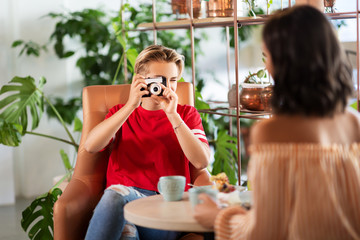 people, communication and friendship concept - female friends drinking coffee and photographing by...