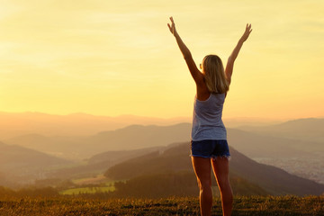 Happy woman with open arms stay on the peak of the mountain 