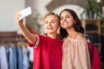 sale, shopping and technology concept - happy female friends taking selfie by smartphone at vintage clothing store