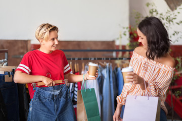 sale, shopping, fashion and people concept - happy young women with takeaway coffee cups choosing...