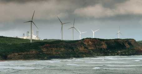 Wind towers at in Southern Australia with moody sky and aluminium smelter in the background.
