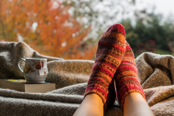 Woman's feet wearing handmade knitted colorful wool socks next to a hot cup of tea in a cozy decor....