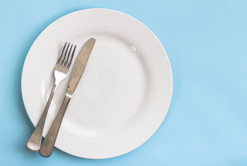 Fototapeta na wymiar Dinner plate, knife and fork isolated on blue backgroud