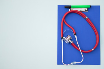 Red stethoscope and green marker pen on a blue clipboard template concept. Medicine Compliance and Exam Background.