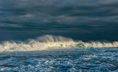 Powerful ocean wave on the surface of the ocean. Wave breaks on a shallow bank. Stormy weather, clouds sky background. Seascape.