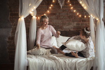 Obraz na płótnie Canvas Teen girl plays with mom on bed, fighting pillows