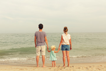 Happy family! Dad, mother and daughter are standing on the seashore. Back view.