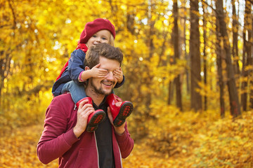 Happy family! The girl closes her dad's eyes with her hands on autumn walk.