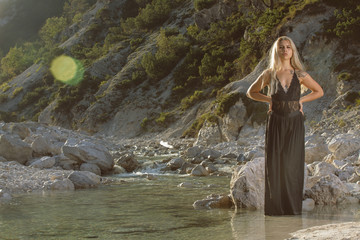 Nice young blonde woman in black dress posing when standing in the river