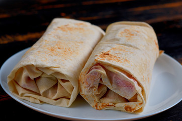 Traditional arabic food - grilled shawarma sandwiches or lavash snacks on the white plate on the dark wooden kitchen background. Eastern cuisine