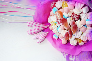 Bouquet of sweets in the pink paper with two hearts on white background