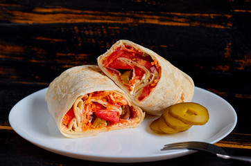 Eastern sandwich or healthy lavash snack with fresh vegetables and sauce on the white plate decorated with silver fork on the black kitchen table. Traditional Iranian food. Arabic cuisine. Side view