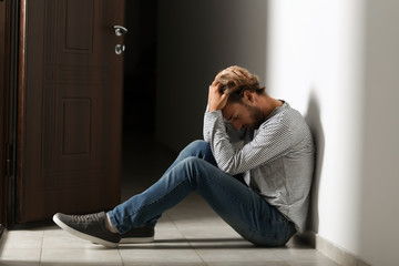 Depressed young man sitting on floor in dark corridor