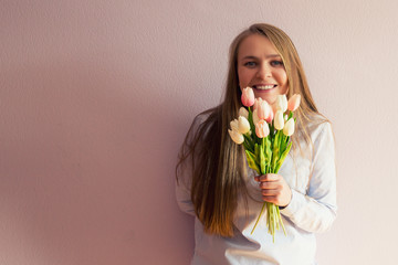 A young beautiful girl with blond long loose hair, keeps spring flowers in the hands of a sunny day. She smiling. Copy space.