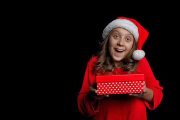 Merry Christmas. A young girl in a red sweater and a Santa Claus hat holds a present - a box