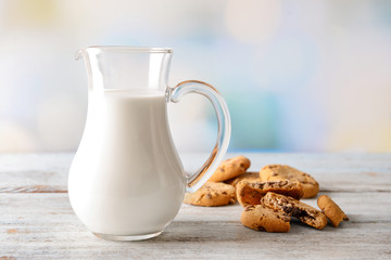 Jug of tasty milk with cookies on wooden table