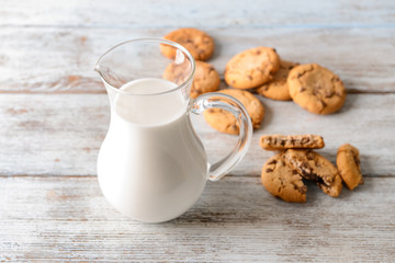Jug of tasty milk with cookies on wooden table