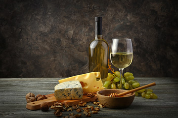 Glass and bottle of white wine with snacks and ripe grapes on wooden table