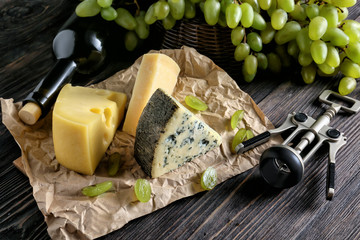 Cheese with bottle of wine and ripe grapes on wooden table