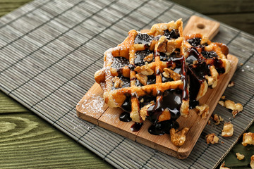 Tasty waffles with chocolate and walnuts on wooden board