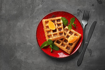 Tasty waffles with cut orange on plate