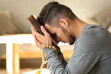 Young Muslim man with Koran praying at home