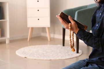 Young Muslim man with Koran praying at home