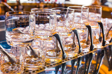 Transparent glasses for alcoholic beverages stand on the bar with a spatula. Yellow lights on the bar, the table reflects the glasses. Service in a restaurant or bar