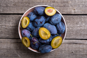 Fresh plums in bowl on wooden table
