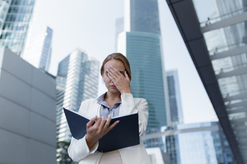 Stressed woman looks in her notebook standing, in the middle of the business centre