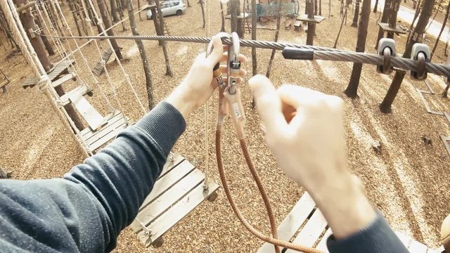 Climbing park attaching safety ropes from wire to wire person POV 4K. Camera on a person's head with a wide view while climbing in adventure park in autumn. Slow motion first person view.
