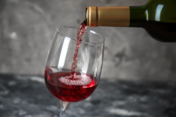 Pouring of red wine from bottle into glass on grey background
