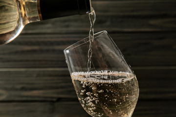 Pouring of wine from bottle into glass on wooden background