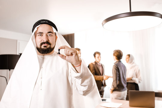 Arab businessman in candora costume holding a pawn standing on the background of colleagues in the office