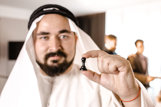 Arab businessman in candora costume holding a pawn standing on the background of colleagues in the office