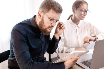 Two young angry business woman man colleagues sit work at white desk with contemporary laptop isolated background. Achievement career concept. Office worker looks at the wristwatch