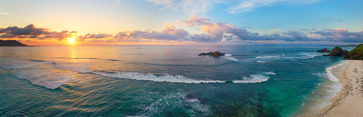 Panoramic view of tropical beach with surfers at sunset.